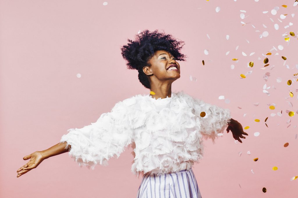 Happy woman with confetti on pink background